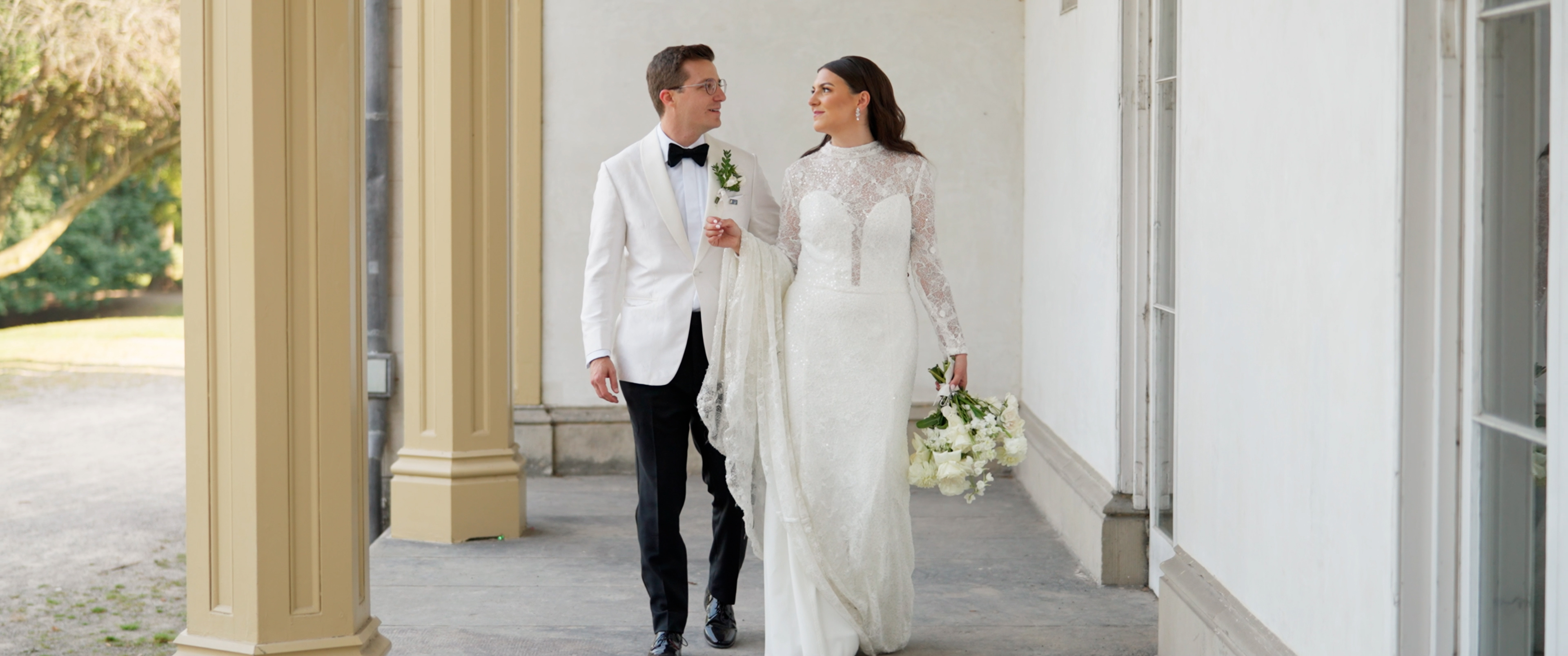 Wedding couple walking through a stone colonnade at a luxury estate