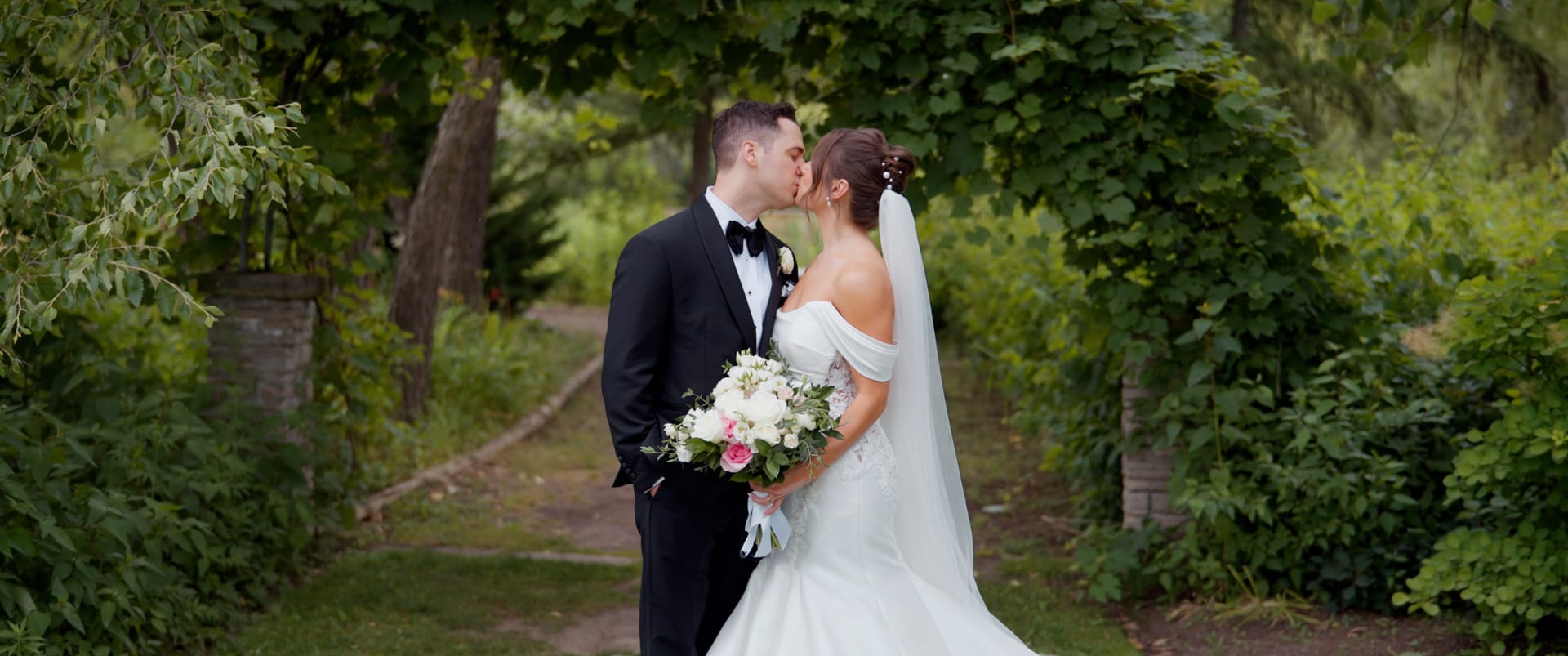 Bride and groom kissing along a tree-lined garden path — documentary wedding film