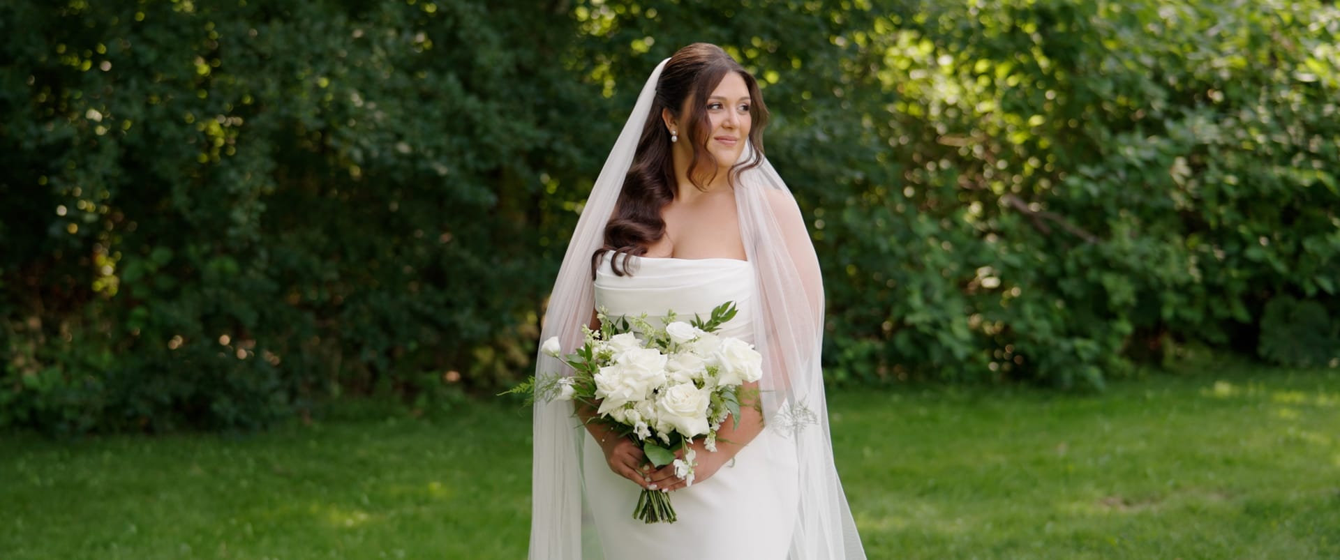 Bride holding her bouquet against a garden hedge — documentary wedding film